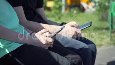 有黑色智能手机的男孩坐在长凳上。 带着手机的小男孩坐在花园里的长凳上。 儿童通过动员交流